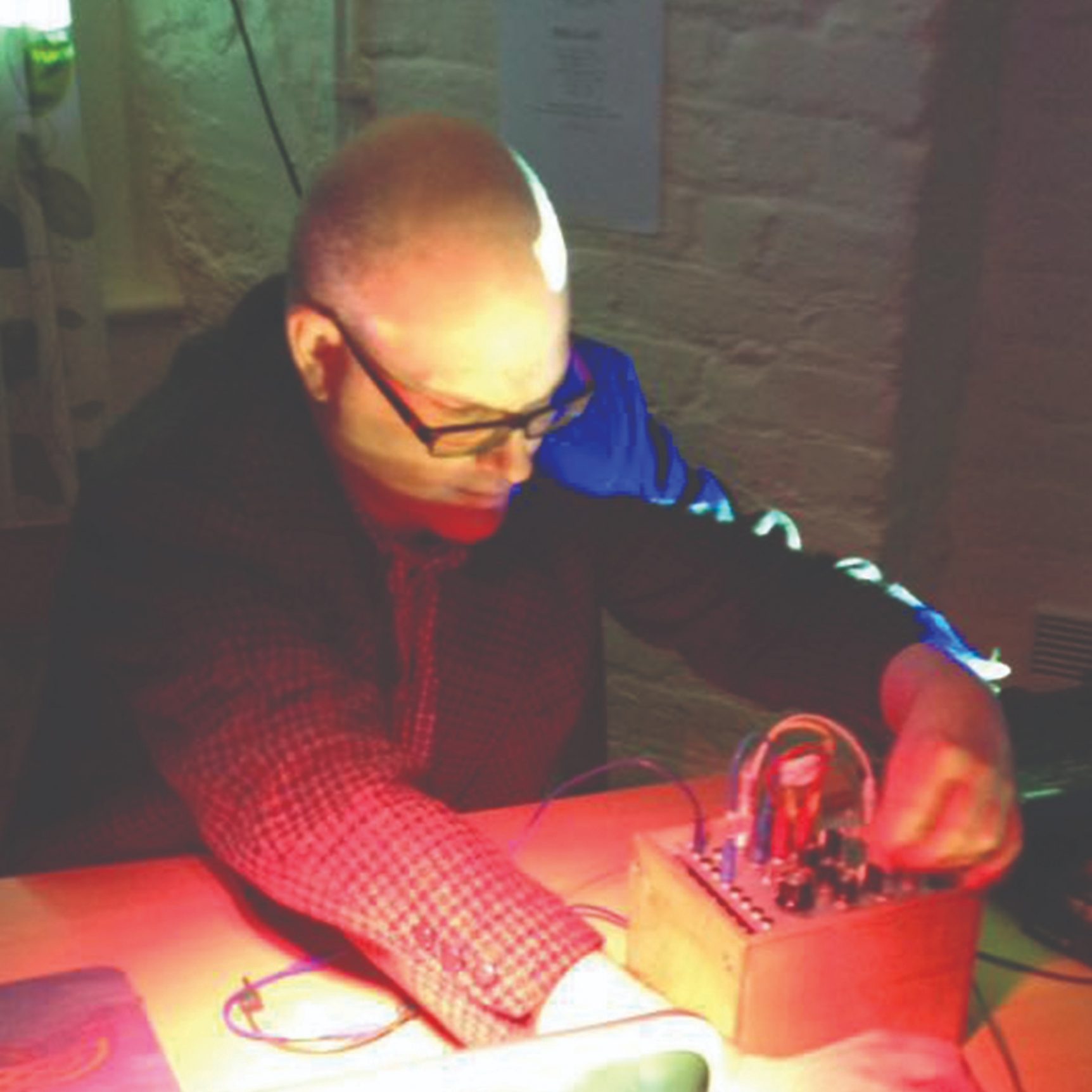 Dafydd Roberts (white man with shaved head, wearing glasses and a jacket) altering the settings on a small, electronic device