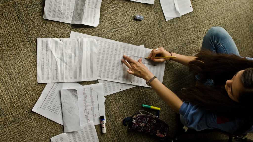 Young girl sitting cross legged on floor, working on scores