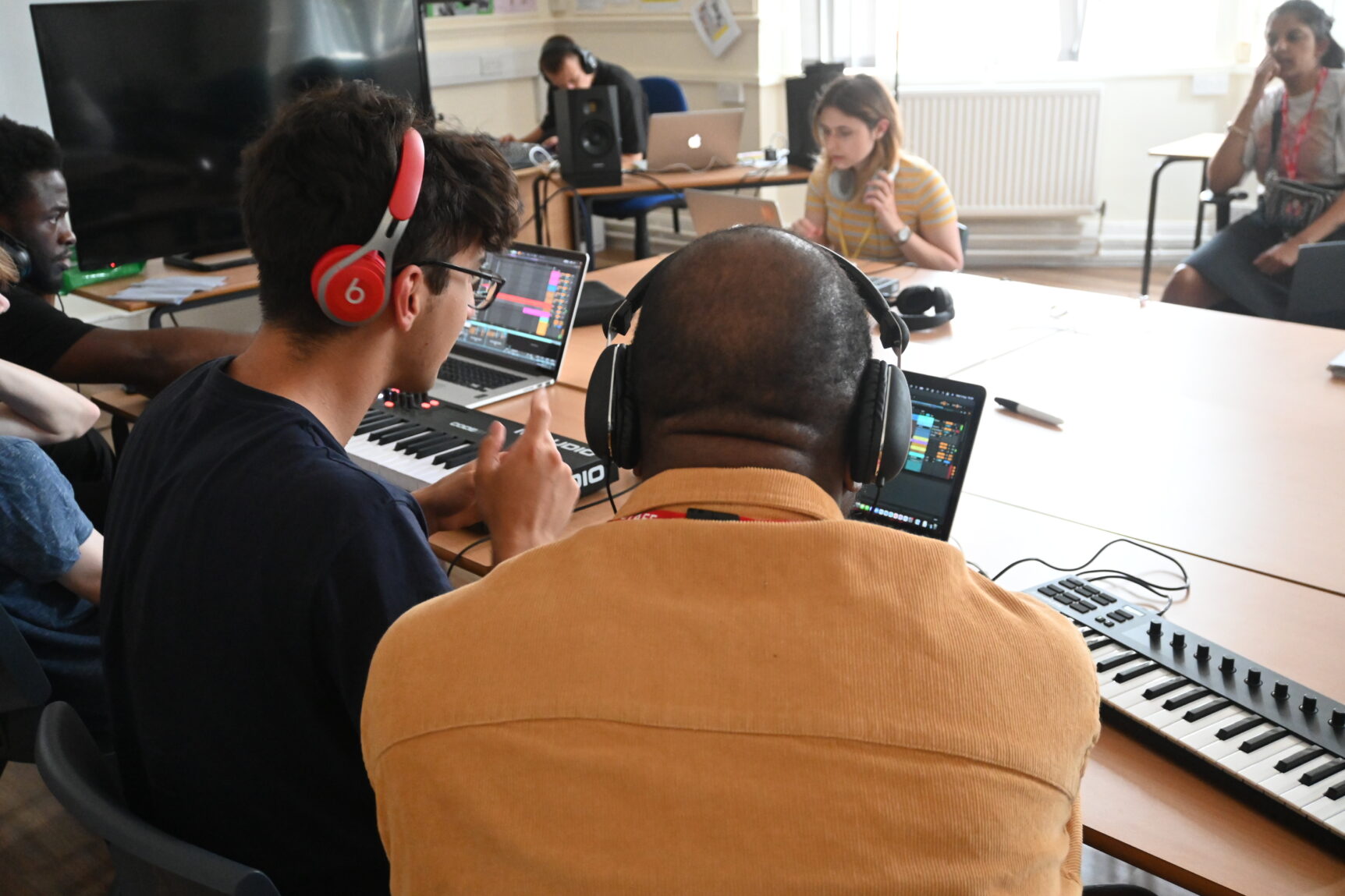 People with headphones sit together around a large table, editing music using computers and software, intently focussing on the task.