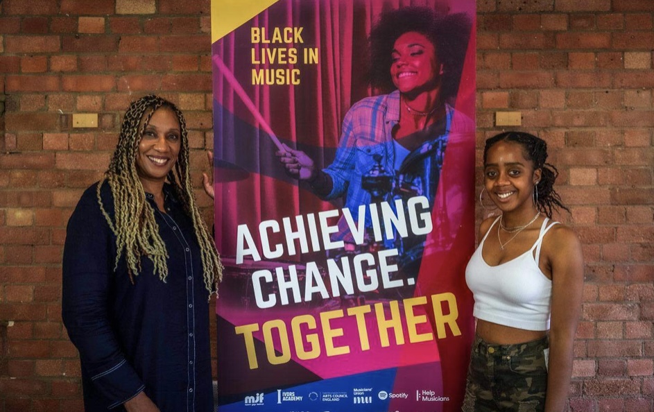 An image of two people, a mentor and a mentee, stood next to a banner reading ‘Black Lives in Music. Achieving Change Together’