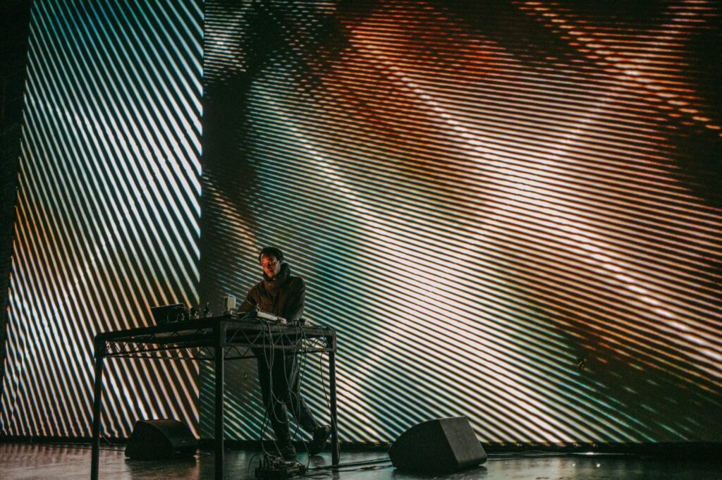 A person performing at a DJ desk in front of a wall of lights.