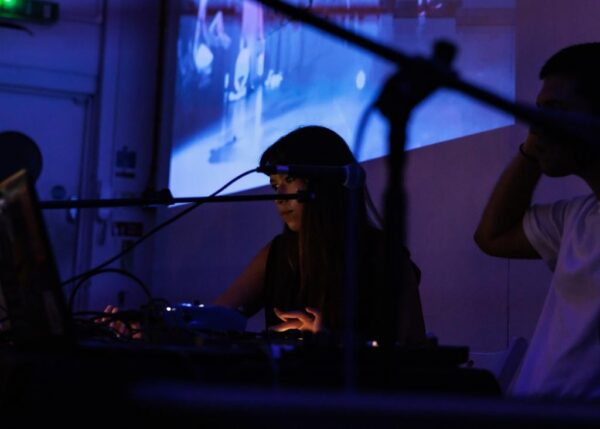 A photograph of composer Sara Rahman performing in a back-lit darkly-lit space.