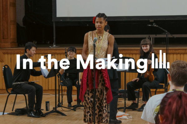 A photograph of a young composer at the Composition School presenting their piece. Behind the young composer are professional musicians who are ready to perform the work. Text overlayed reads “In the Making”